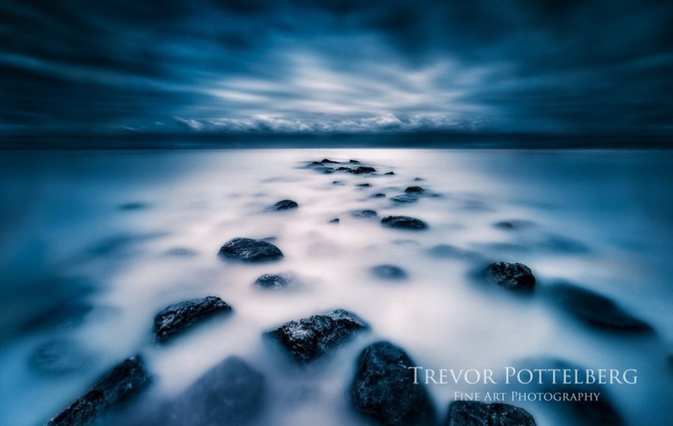 A dreamy slow shutter photo of rocks emerging from the water under stormy skies