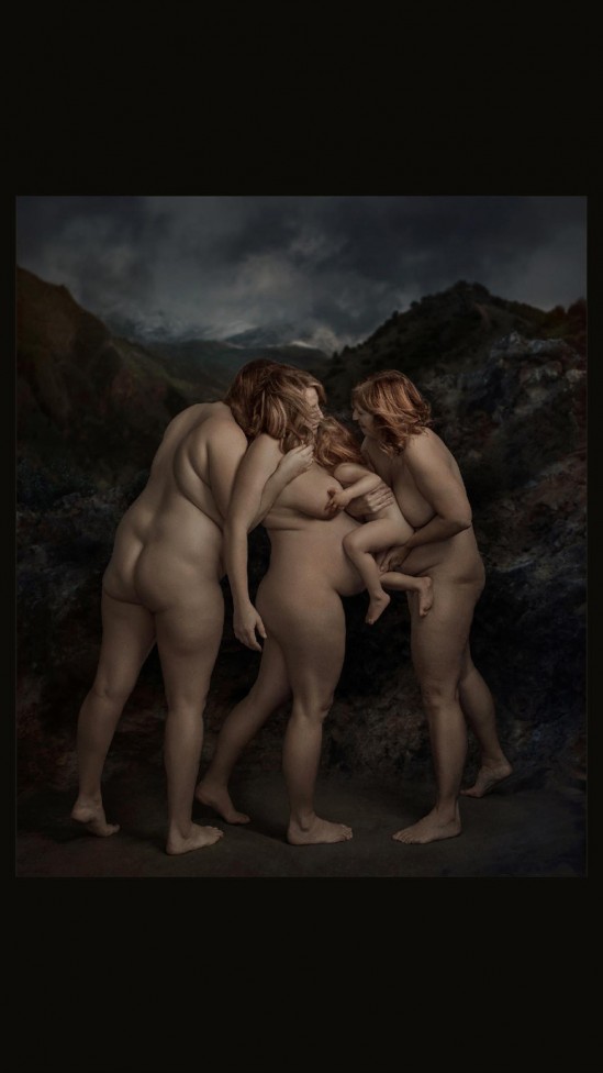 An image of 3 naked women from behind, one is holding a baby. Stormy clouds gather over mountains in the distance.