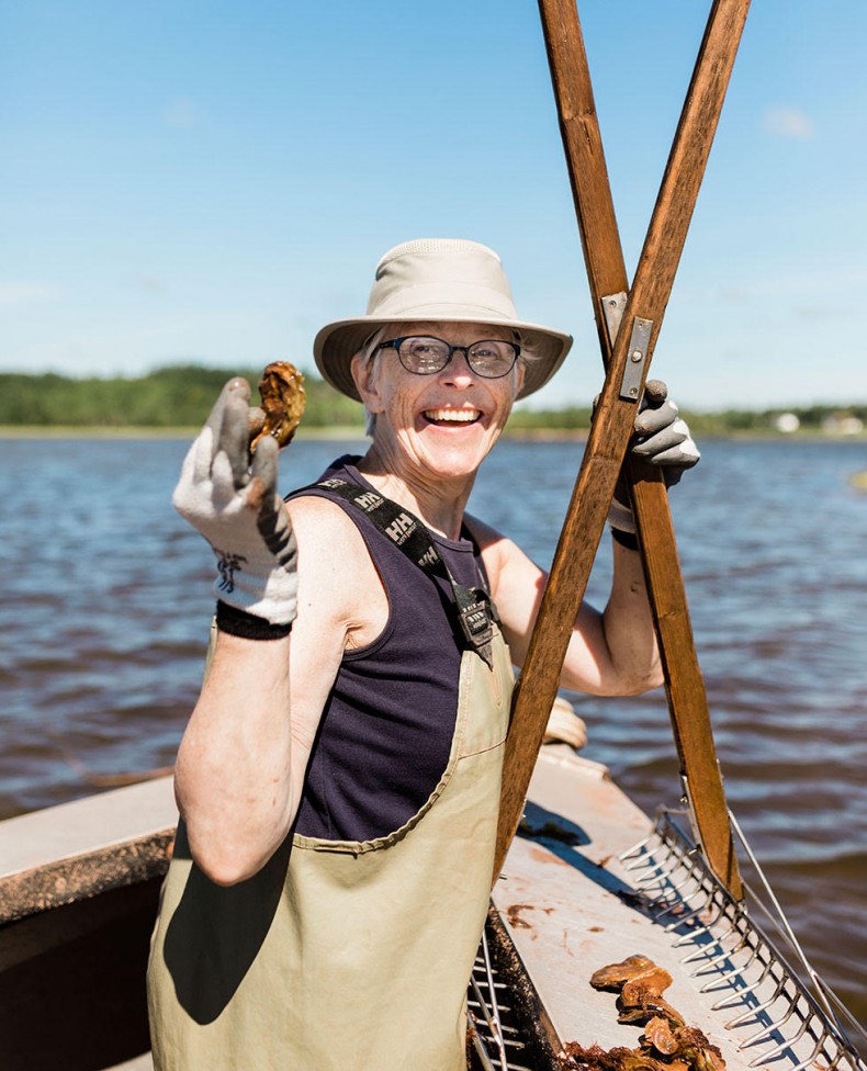 Photographer Debbie Brady of Oyster Art, holding an oyster and oyster tongs on a boat.