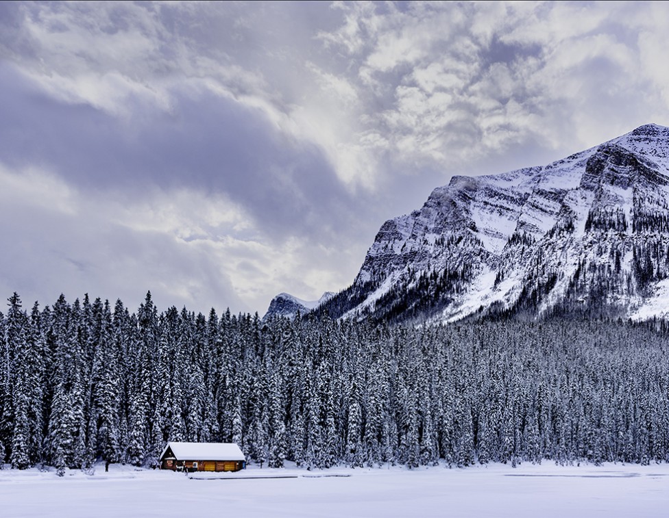 A snowy landscape scene showing a cabin in the mountains.