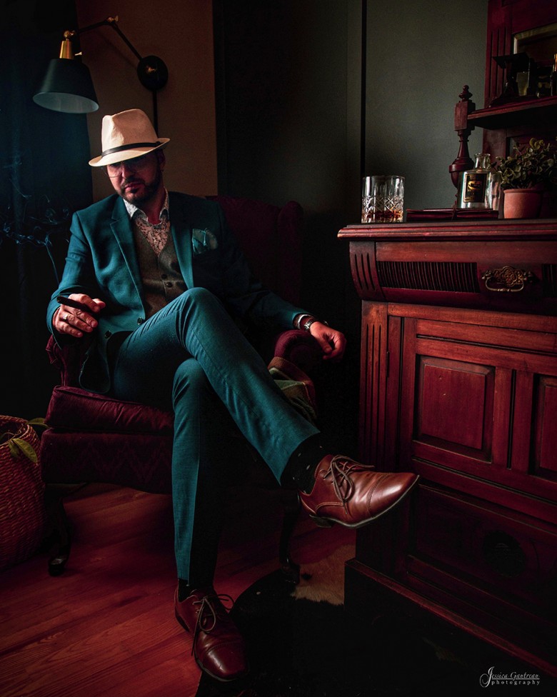 A portrait of a man in a suit enjoying a cigar and whiskey