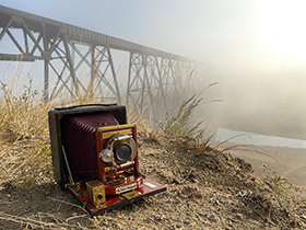 a large format camera sits in front of a foggy train bridge across a coulee.