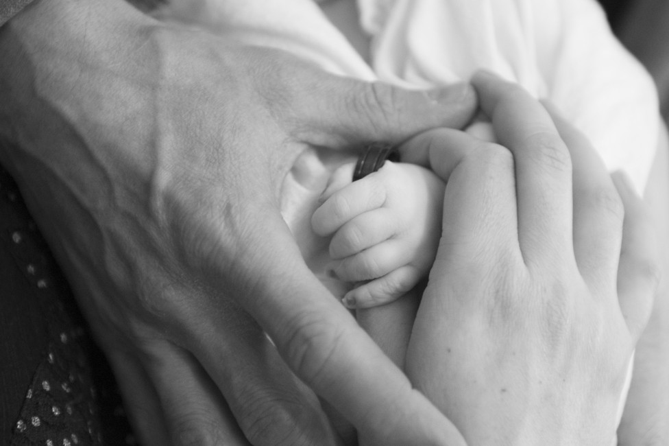 A black and white photo of the parents' hands framing a newborn's hand